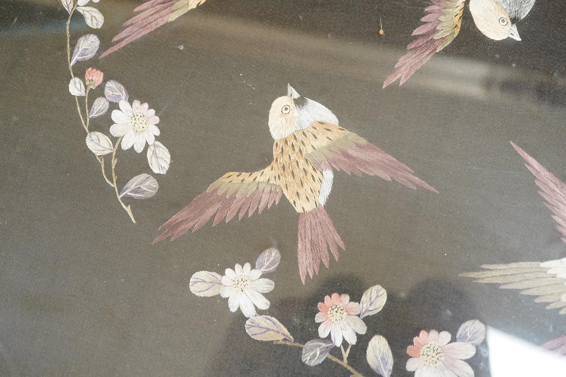 Two Chinese polychromed silk embroidered panels, early 20th century, one on a black silk ground of birds and flowers, the other on a red background of flowers and a monochrome silk embroidered panel of birds and flowers,